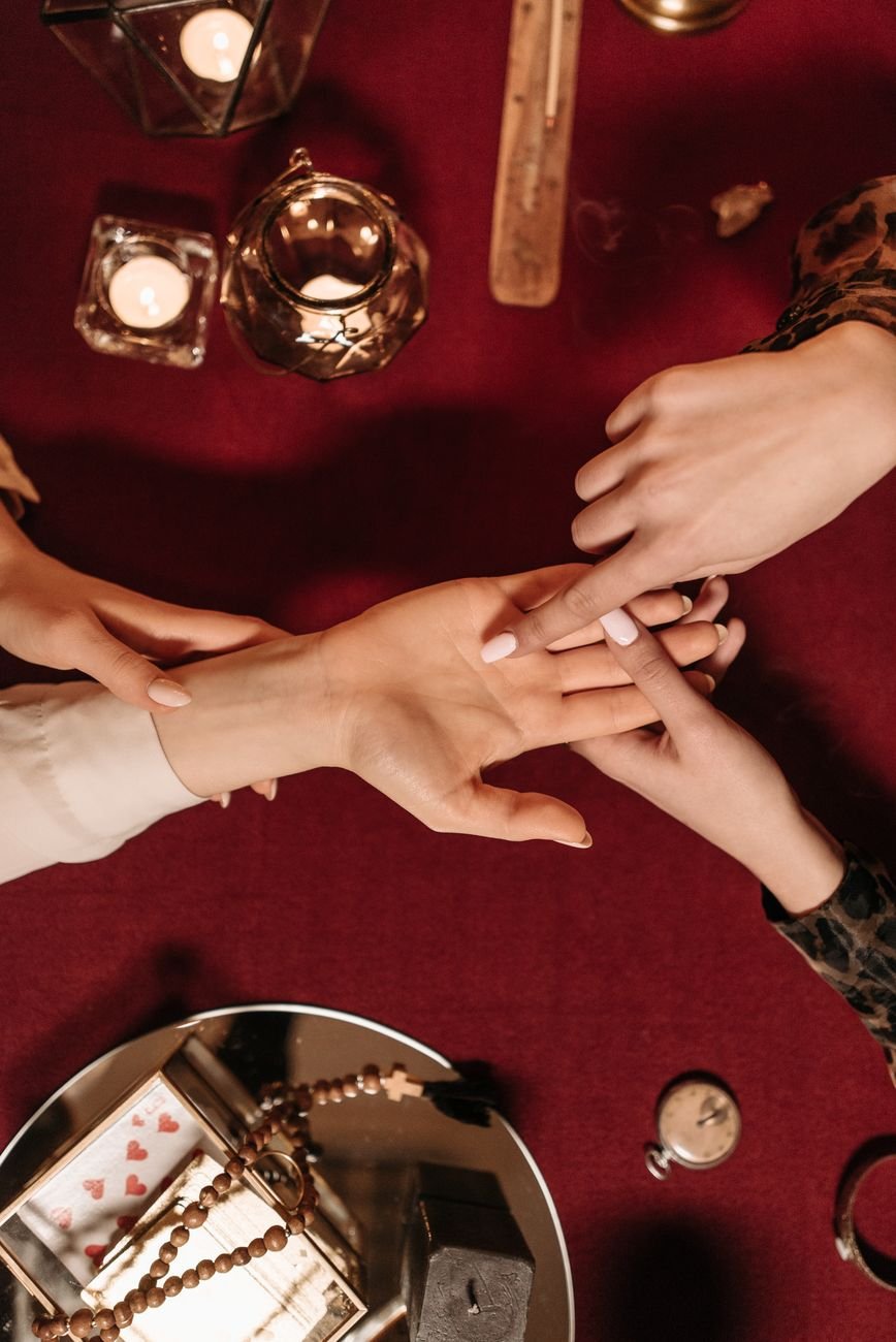 Top view of a mystical palm reading setup with candles and tarot on a velvet table.